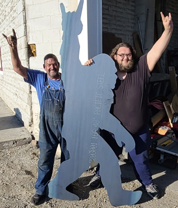 Dad and Son grinning outside the shop, holding a giant steel Sasquatch cutout