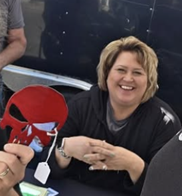 Mom smiling at the Mack Made booth, holding a red powder-coated steel piece