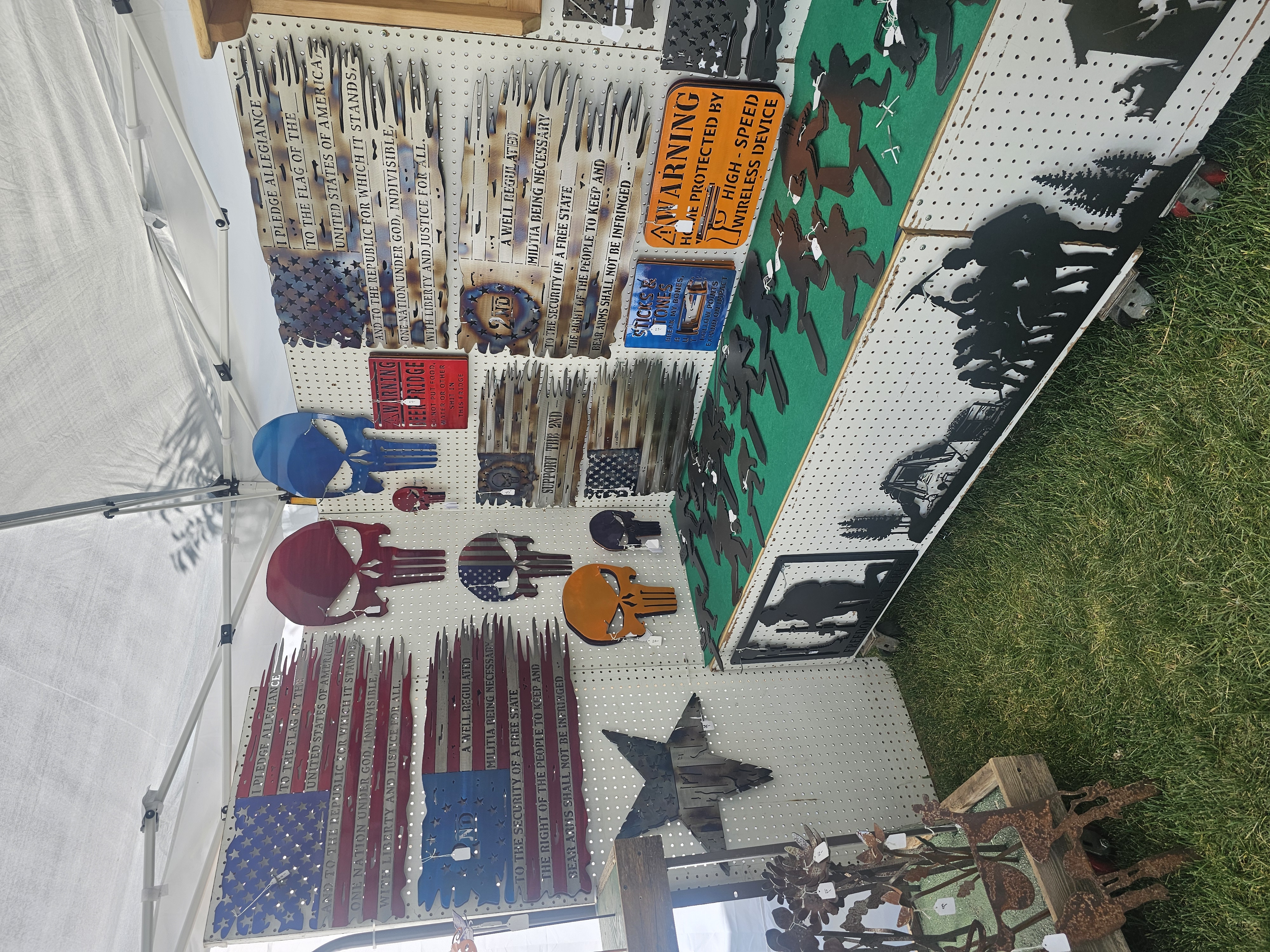 Display wall at a market booth featuring patriotic metal art, including American flags, Punisher skulls, and military-themed signs.